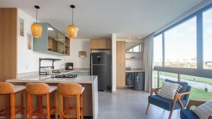 A modern kitchen with a central island, bar stools, a refrigerator, and a view of the outdoors. - Apartment in Condominium With Pool Vll0002 (Maraú)