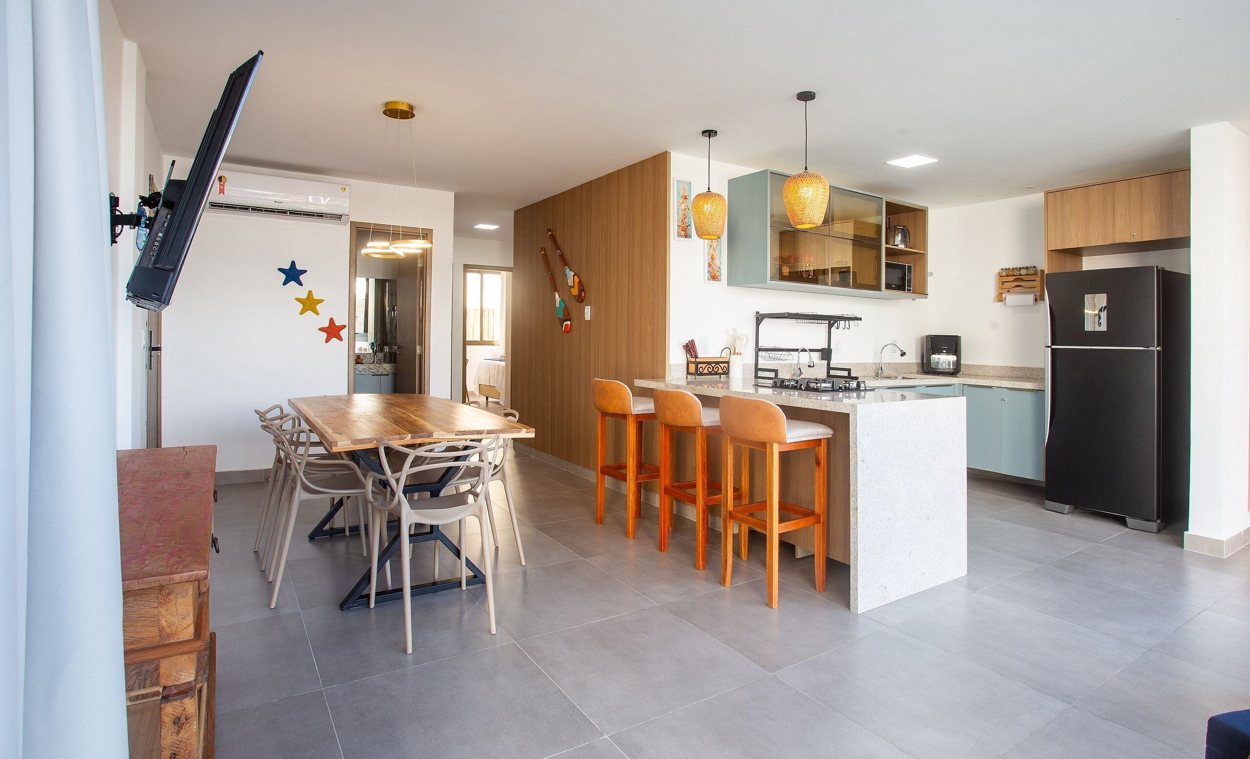 A modern kitchen with a central island, bar stools, a dining table with chairs, and a refrigerator.