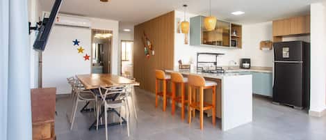 A modern kitchen with a central island, bar stools, a dining table with chairs, and a refrigerator.