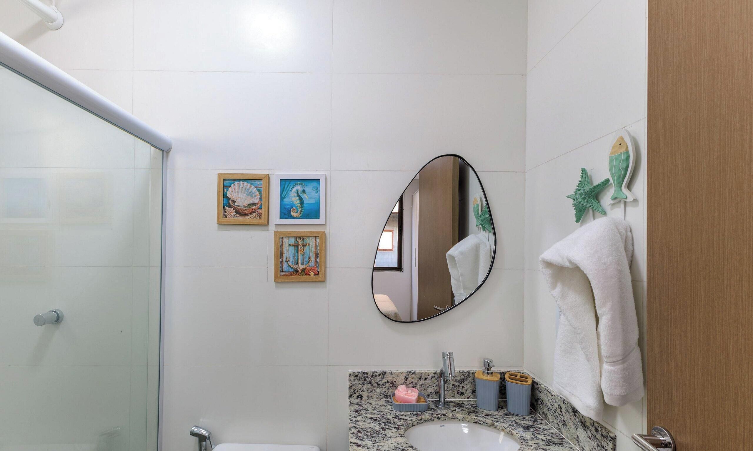 Casa de banho com cabine de duche em vidro, lavatório com bancada de granito e espelho com pintura de cavalo-marinho.