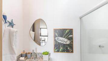 A bathroom with a marble countertop, a sink, a mirror, a towel rack, a framed thankfulness sign, and a shower area.