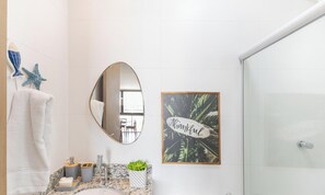 Un baño con encimera de mármol, lavamanos, espejo, toallero y zona de ducha.