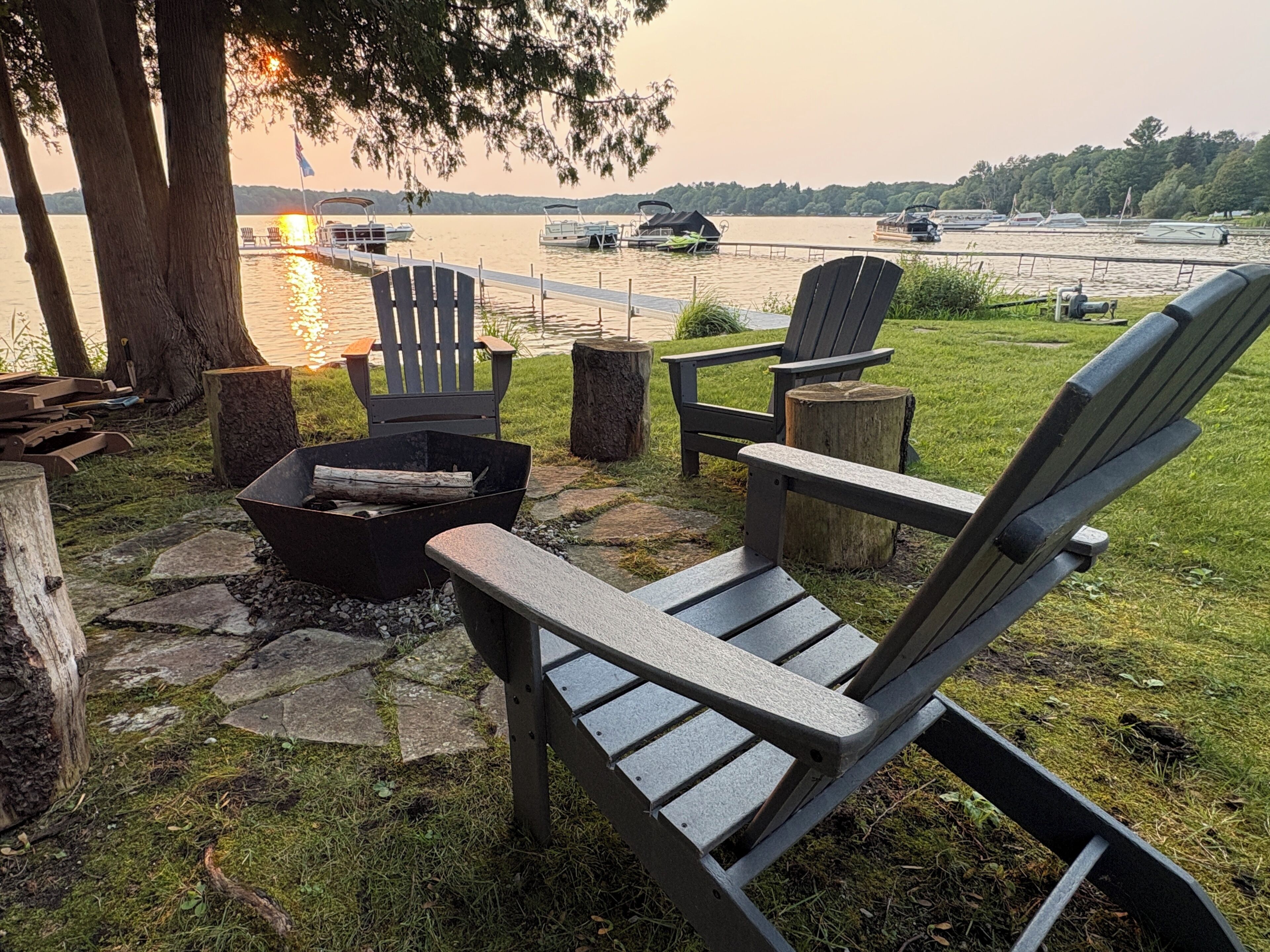 Et opholdsområde ved søen med Adirondack-stole, en bålplads og udsigt til både på vandet.