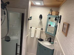 A bathroom with a glass shower enclosure, a vanity with a sink, a mirror, and a towel rack. - Cozy 1-bedroom vacation cottage on beautiful Lake Ann (Lake Ann)
