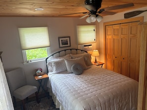 A bedroom with a bed, bedside table, chair, and a wooden wardrobe. - Cozy 1-bedroom vacation cottage on beautiful Lake Ann (Lake Ann)