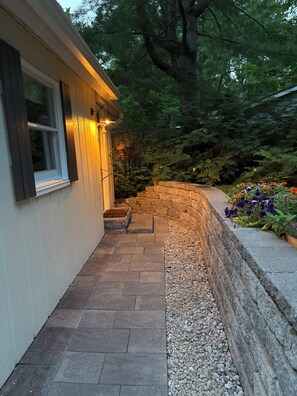 A pathway leading to a house with a stone retaining wall and a garden with various plants and flowers.