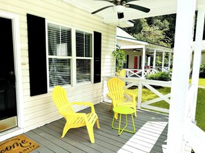 Eine Veranda mit zwei gelben Stühlen und einem kleinen Tisch, einem weißen Deckenventilator und einem überdachten Bereich mit Geländer.