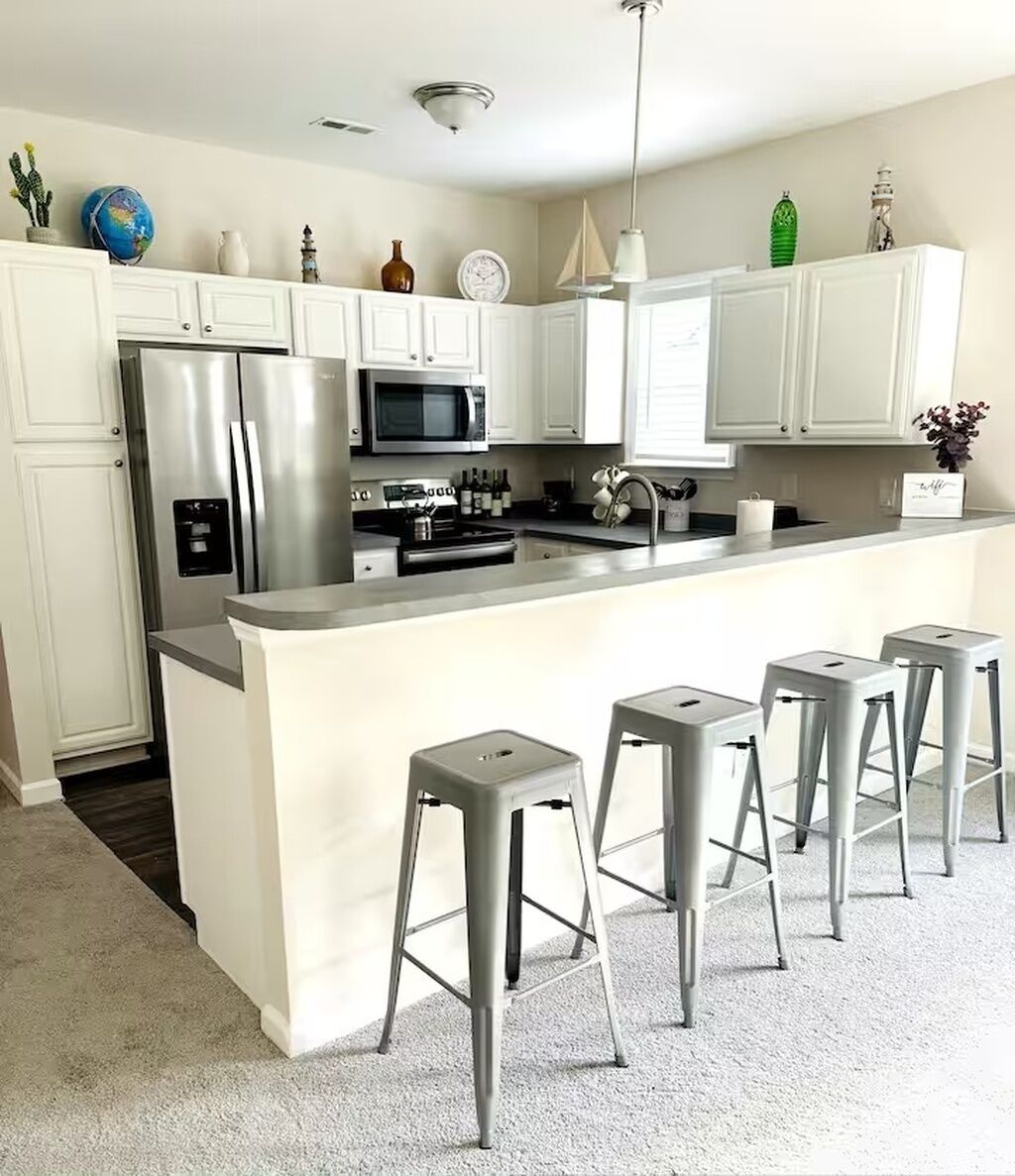 Een moderne keuken met witte kastjes, roestvrijstalen apparatuur en een centraal eiland met barkrukken.