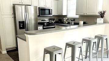 Een moderne keuken met witte kastjes, roestvrijstalen apparatuur en een centraal eiland met barkrukken.