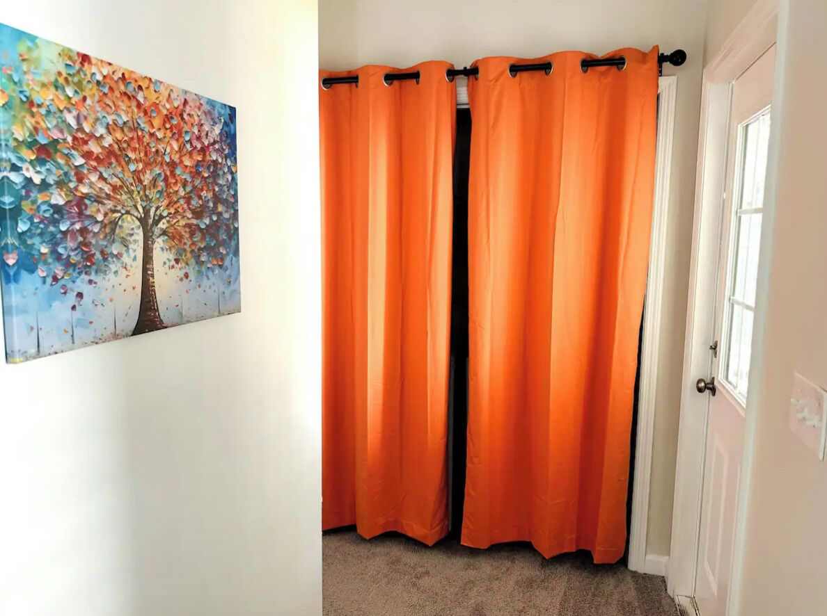 Quarto com porta, pintura de uma árvore e cortinas laranja.
