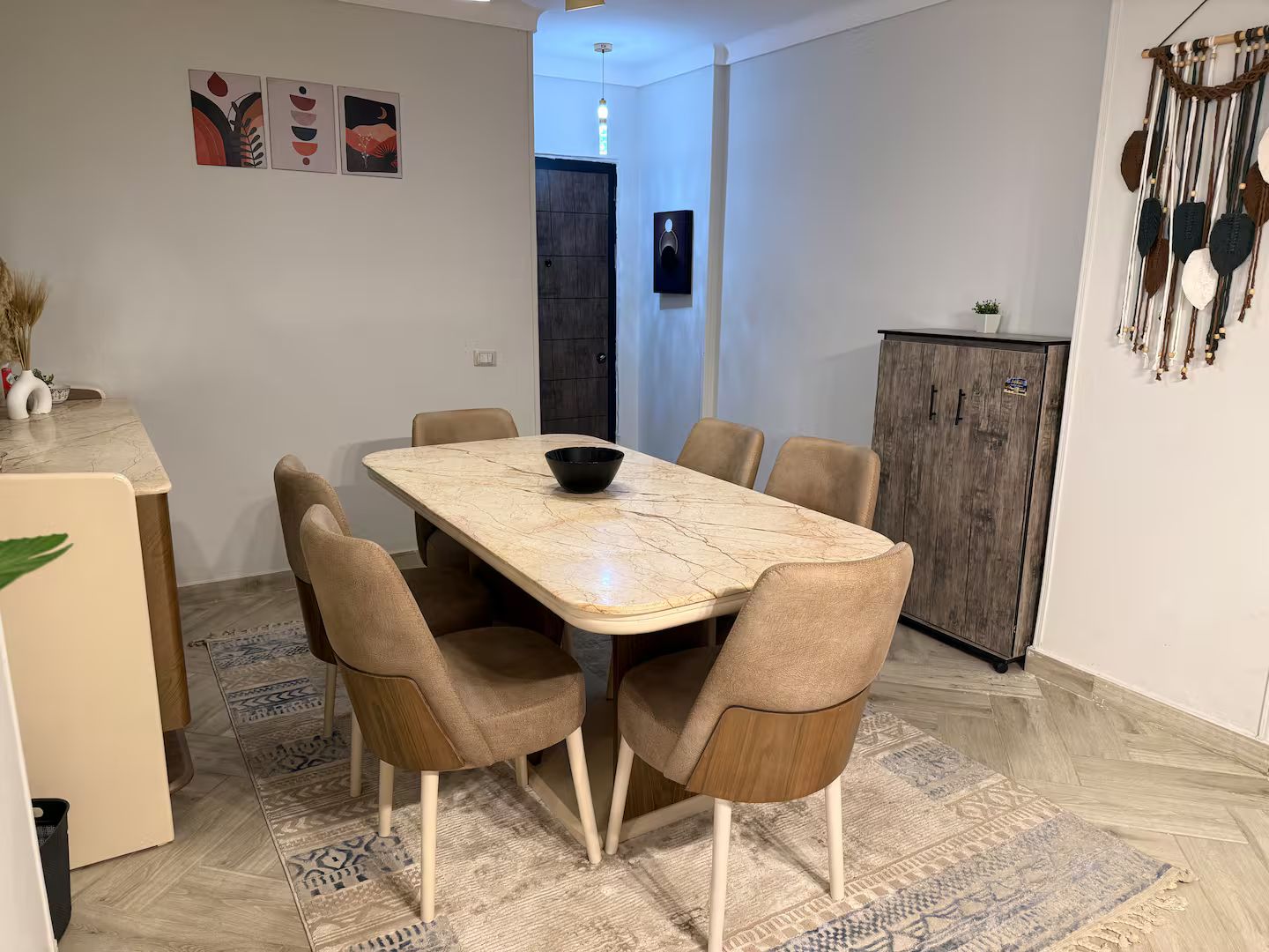 A dining area with a marble table, six chairs, a bowl, a cabinet, and a patterned rug.