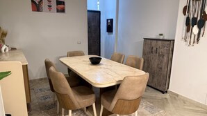 Een eetruimte met een marmeren tafel, zes stoelen, een schaal, een kast en een kamerbreed tapijt.