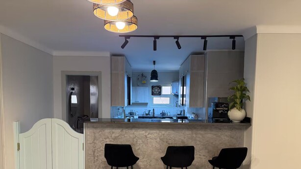 Een moderne keuken met een centraal eiland, barstoelen en een hangende lamp.