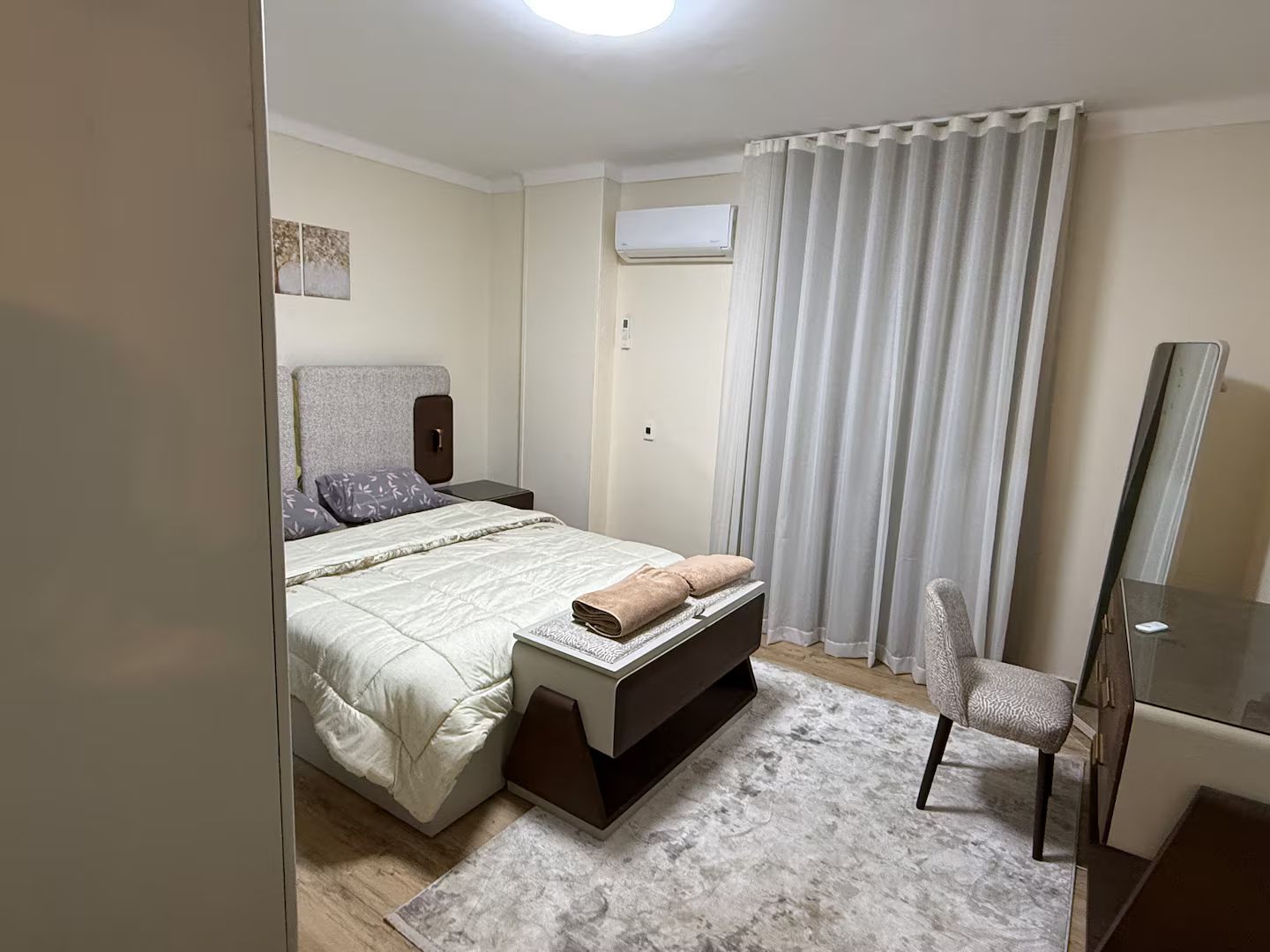 Ein Schlafzimmer mit Bett, Nachttisch, Stuhl und Spiegel.