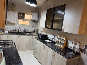 A modern kitchen with a gas stove, black countertops, wooden cabinets, and a built-in oven. - Luxurious Apartment in best location in Dokki (Giza)