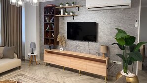 Een moderne woonkamer met een flatscreen televisie, een houten dressoir en een grote potplant.