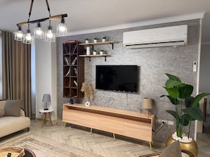 Un salon moderne avec un téléviseur à écran plat, une console en bois et une grande plante en pot.