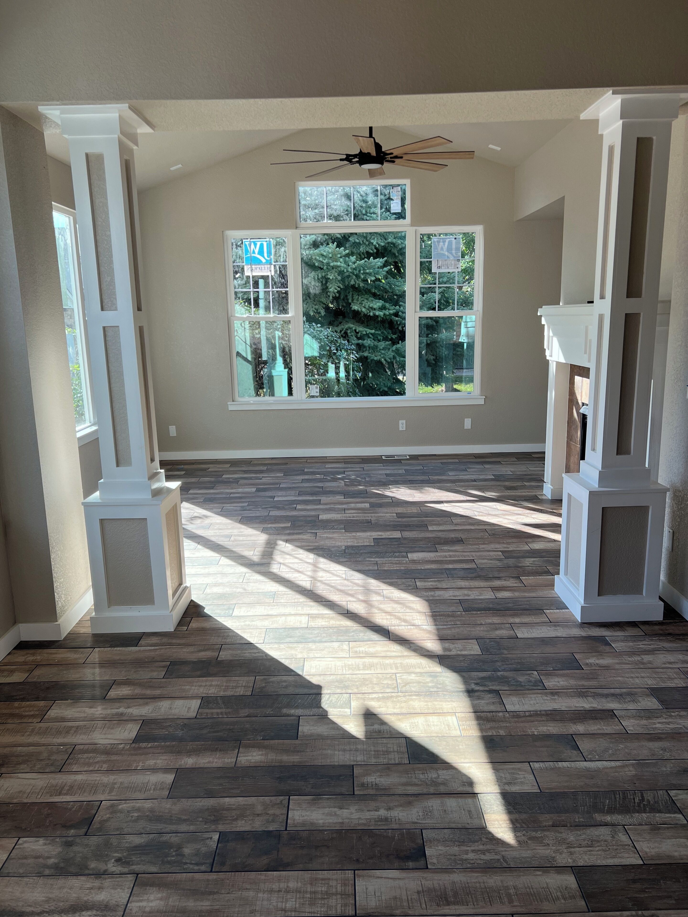 A spacious room with a large window, wooden flooring, and a ceiling fan.