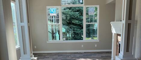 A spacious room with a large window, wooden flooring, and a ceiling fan.