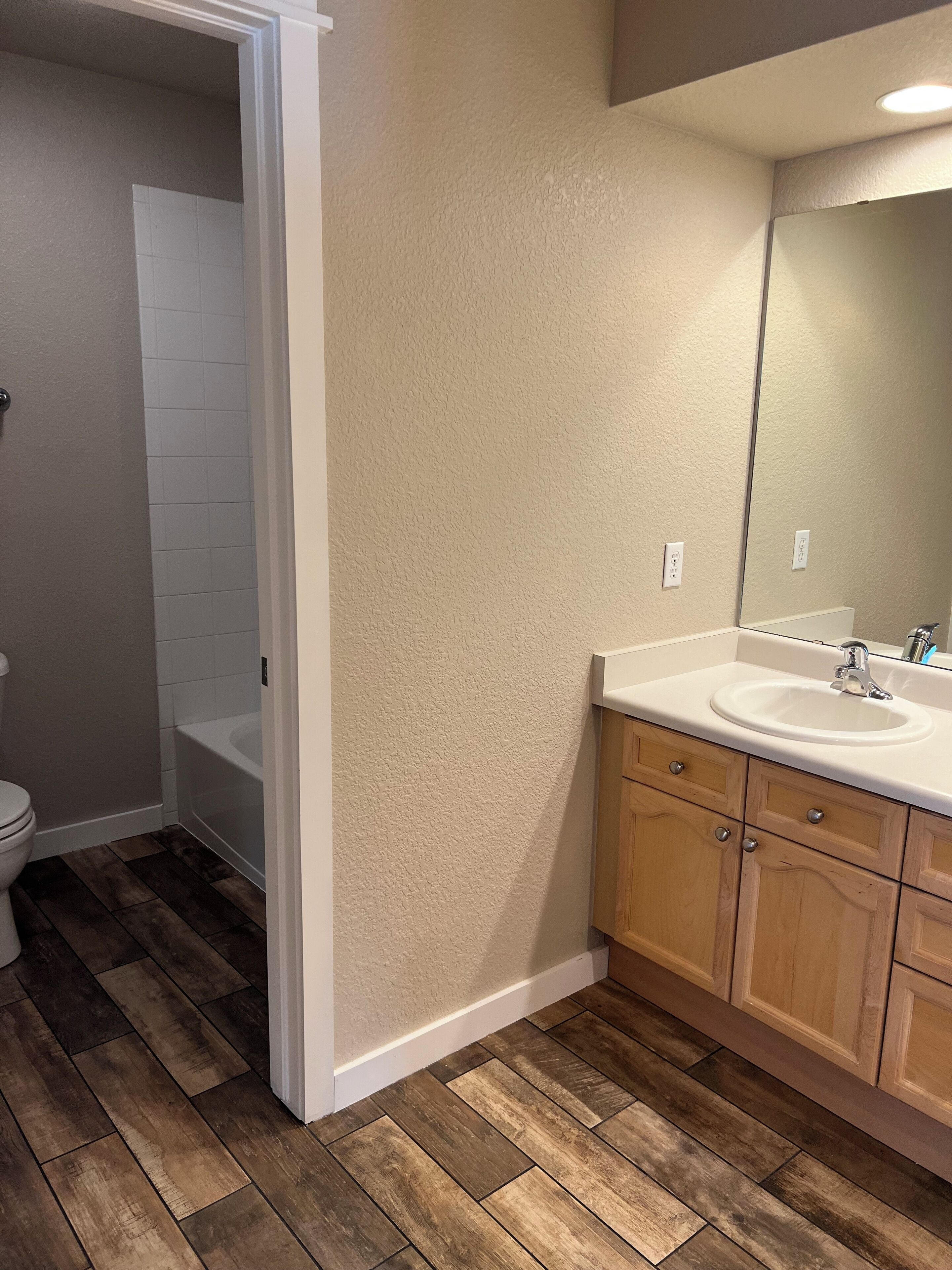 A bathroom with a wooden floor, white tiles, a bathtub, and a sink with wooden cabinets.