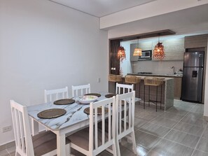 Eine moderne Küche mit Essbereich, ausgestattet mit einem Marmortisch, weißen Stühlen und einem Edelstahlkühlschrank.