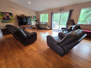 A spacious living room with a large flat-screen TV, leather sofas, and a sliding glass door leading to an outdoor area.
