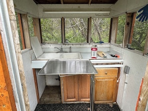 A compact kitchen with a sink, wooden cabinets, and a window overlooking greenery. - Sterling Riverfront Retreat - Private Kenai River Access (Sterling)
