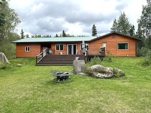 A log cabin with a front porch, a deck, and a large rock in the foreground. - Sterling Riverfront Retreat - Private Kenai River Access (Sterling)
