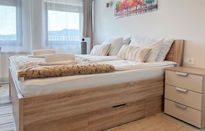 Habitación de hotel con cama, mesita de noche, unidad de aire acondicionado montada en la pared y un cuadro.