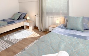 Ein Schlafzimmer mit zwei Betten, einem Nachttisch, einer Lampe, einem Fenster mit Vorhängen und einer Heizung.