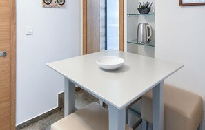 Ein kleiner, weißer Tisch mit einer Schale darauf, eine Glaskonsole mit einem Wasserkocher und eine Tür mit Lichtschalter.