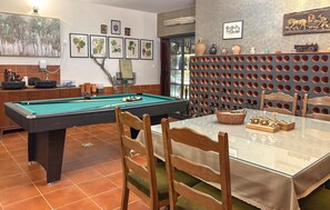 Ein Billardtisch mit Stühlen, ein Esstisch mit einem Korb und Teekannen sowie gerahmte Kunstwerke an den Wänden.