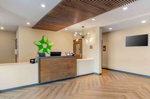Un'area reception con scrivania in legno, un'opera d'arte astratta verde, un lampadario moderno e un televisore a schermo piatto montato a parete.