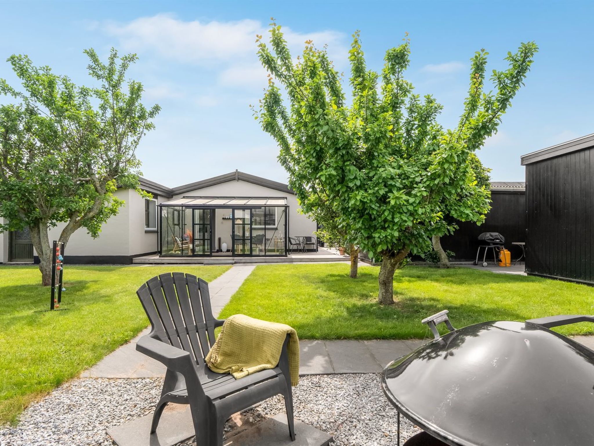 A modern house with a glass patio, a barbecue grill, and a lawn.