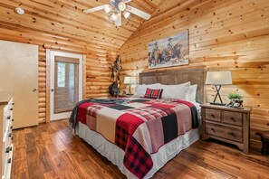 Ein Schlafzimmer einer Holzhütte mit einem Bett, Nachttischen, einem Deckenventilator und einem Bild an der Wand.