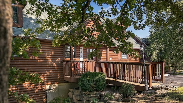 A wooden cabin with a porch, a stone wall, and a small bush.