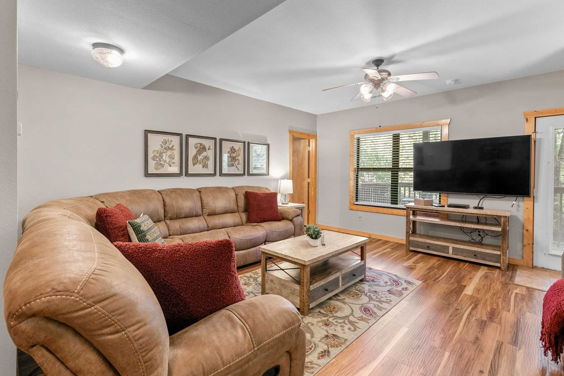 A living room with a leather sofa, a coffee table, a TV on a wooden stand, and framed botanical prints on the wall.