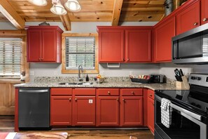A kitchen with red cabinets, a granite countertop, a stainless steel sink, a microwave, and an oven. - Spacious Cabin Sleeps 14 - Two Living Areas - Indoor Pool, Pet Friendly, Branson Woods Resort - 17 (Branson)