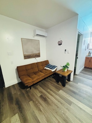 Uma sala de estar com sofá marrom, mesa de centro, pintura e ar condicionado.
