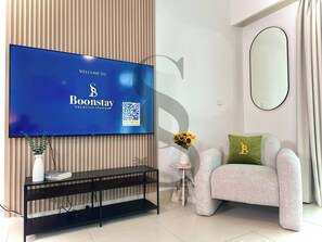 A modern living room with a flat-screen TV mounted on a wooden wall, a sofa with a cushion, a small side table with a vase of flowers, and a console table with a plant and books. - Luxury 2Br Dubai Fountain and Dubai Mall 5 Min (Dubai)
