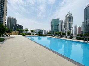 A swimming pool with lounge chairs and a cityscape in the background. - Luxury 2Br Dubai Fountain and Dubai Mall 5 Min (Dubai)