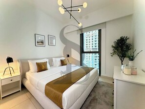 Ein modernes Schlafzimmer mit einem großen Bett, Nachttischen, einem Schreibtisch mit einer Pflanze und einem Fenster mit Blick auf Gebäude.