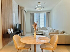 Ein modernes Wohnzimmer mit einem runden Holztisch, zwei gelben Stühlen, einem beigen Sofa und einem Fernseher auf einem dunklen Holzschrank.