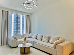 A modern living room with a sectional sofa, a round coffee table, and a contemporary light fixture. - Discounted Luxury 1Br 4 sleeps Dubai Creek Harbour (Dubai)