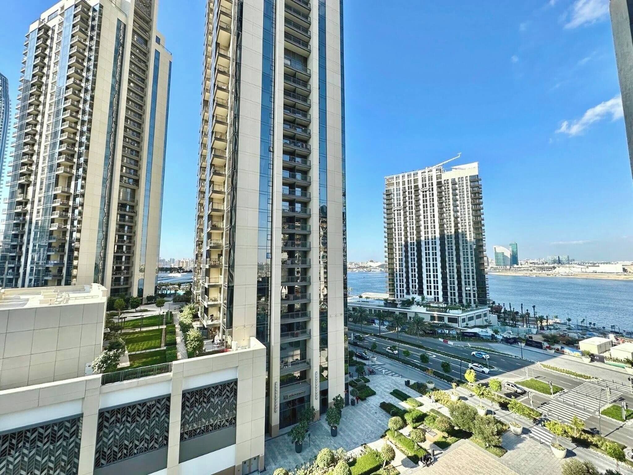 A high-rise residential building with multiple balconies, a waterfront view, and a well-maintained surrounding area with greenery.