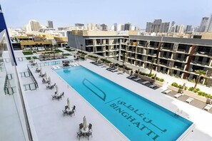 A rooftop pool area with lounge chairs and a pool with 'BINGHATTI' branding, surrounded by high-rise buildings. - Lowest Price  Amazing City  View Luxury 1 Br (Dubai)