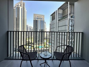 Ein Balkon mit zwei Stühlen und einem kleinen Tisch, mit Blick auf eine Skyline mit Hochhäusern und einem Schwimmbecken.