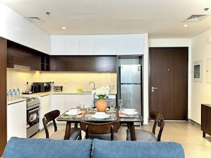 A modern kitchen with white cabinets, a built-in oven, and a refrigerator. There is a dining table set with plates, glasses, and a vase of flowers. - Amazing View Special Discount Luxury 1 Br Apt (Dubai)