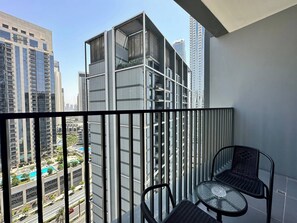 Un balcón con vistas a edificios altos, una mesa de vidrio y dos sillas.