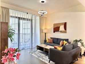 A modern living room with a grey sofa, a coffee table, and a painting on the wall. - Amazing View Special Discount Luxury 1 Br Apt (Dubai)